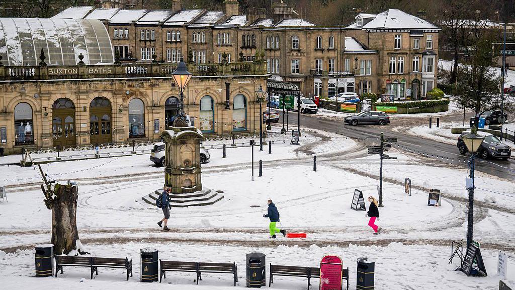 An overhead shot of a public square in Buxton. Two children can be seen - one dragging a snow sledge as snow on the ground has turned slushy