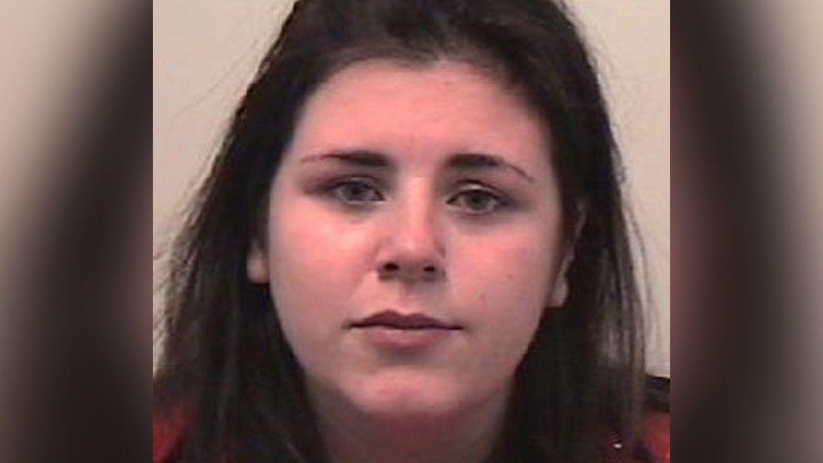 A woman with long, dark hair wearing a red top, positioned against a plain light-coloured background.