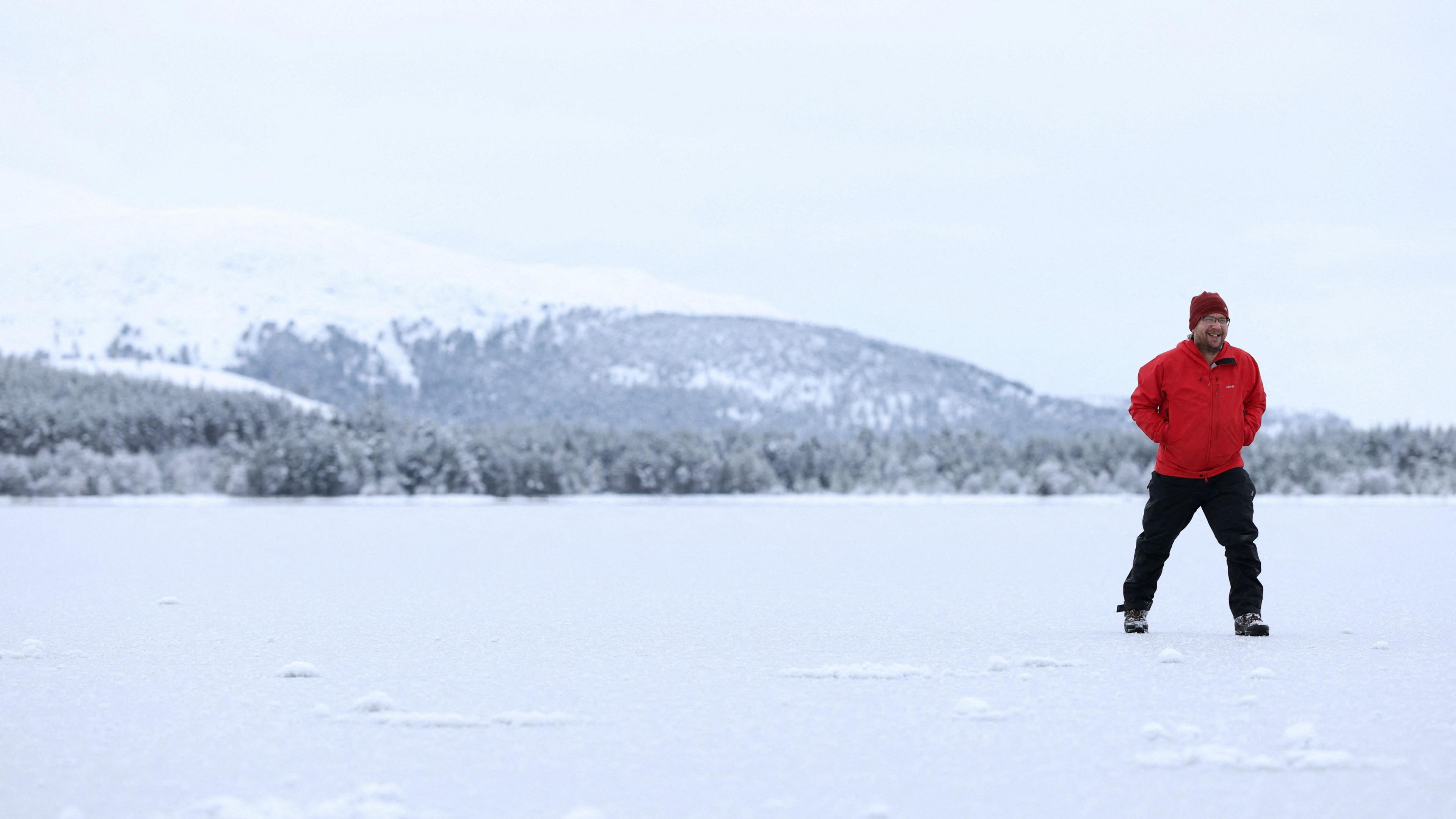 A man wearing a red jacket stands to the right of the frame - the ground is covered in ice and snow