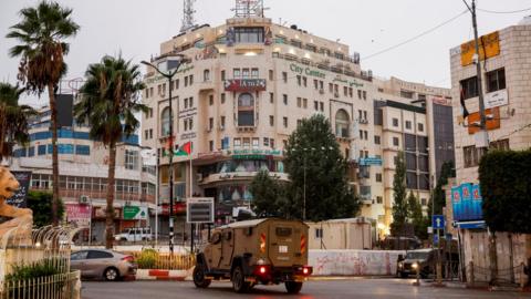 An Israeli military vehicle moves in a street outside the building in Ramallah, in the Israeli-occupied West Bank, where Al Jazeera's office was located before it was ordered to close (22 September 2024)