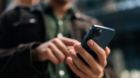 A man wearing dark clothes typing on a smartphone.