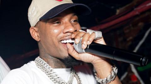 Rapper Tory Lanez seen holding a microphone at an event. He has on multiple diamond chains, rings and a silver diamond bracelet.