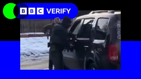 Two federal officers near a burgundy car, one is leaning through the drivers window and the other is in front of car holding a car