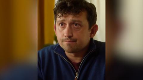 A man in a dark blue zip top with a sceptical look on his face