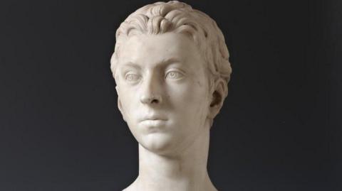 The bust is made from marble and shows the head of a young man, Sir John Gordon. The sculpture is photographed against a black background.
