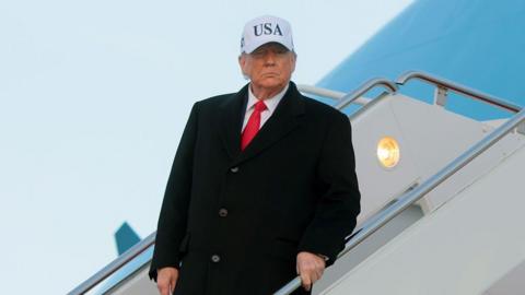 Donald Trump wears a white baseball hat emblazoned with USA and a coat while walking down the air stairs after landing on Air Force in Detroit, Michigan.