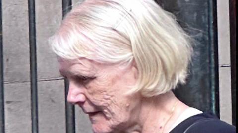 a woman with white/blonde hair in a dark top, pictured outside a court building
