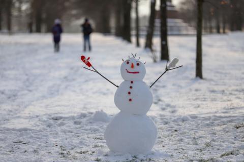 Small snow man stands with stick arms raised surrounded by more snow