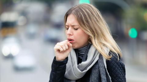 A stock image of a woman coughing into her hand.