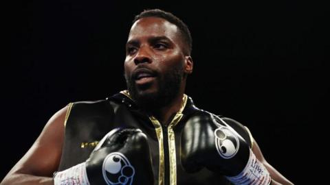 Lawrence Okolie in black boxing gloves and sleeveless black and gold zip-up top