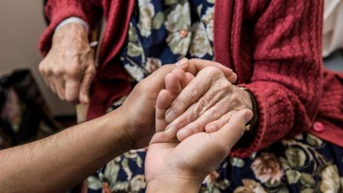 A young carers hand holds an elderly hand gently