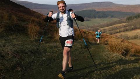 Thomas Smith hiking in hills, looking at the camera and smiling