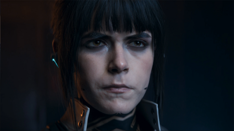 Screenshot shows a photo-realistic rendering of Kiernan Shipka's character, dimly lit, with a stern expression on her face. She wears a high-necked jacket and an earpiece with a microphone stretching towards her mouth.