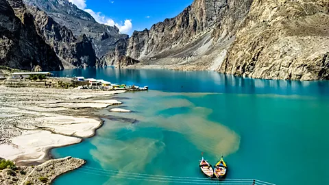 Two small boats float on Lake Attabad in Pakistan with steep mountains on either side (Credit: Getty Images)