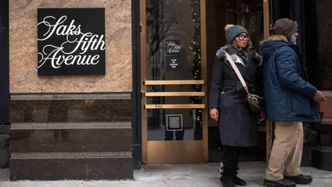 Two people wearing winter clothing leave a Saks Fifth Avenue store.