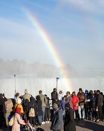 Tourists crowd in front of a rainbow at Niagara Falls.
